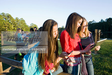 Group of pre-teens sitting on fence, looking at tablet computers and cellphones, outdoors, Florida, USA