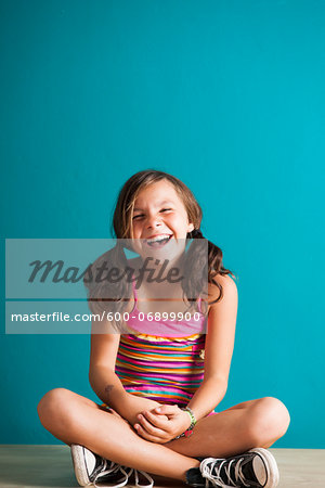 Portrait of girl sitting on floor, laughing, Germany