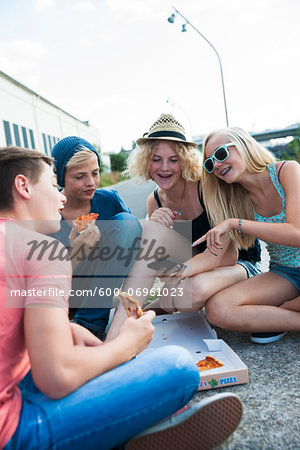 Group of Teenagers sitting on ground outdoors, eating pizza and hanging out, Germany