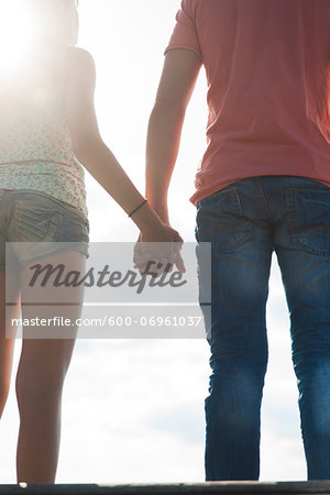 Backview of teenage boy and teenage girl holding hands standing outdoors, Germany