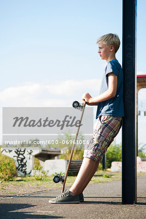 Portrait of boy outdoors with skateboard, standing on street, Germany