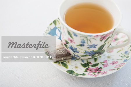 Cup of tea in pretty floral cup with saucer and used tea bag, on white background, studio shot