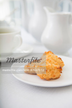Plate of coconut macaroons, pastries with cup of tea and teaset, studio shot