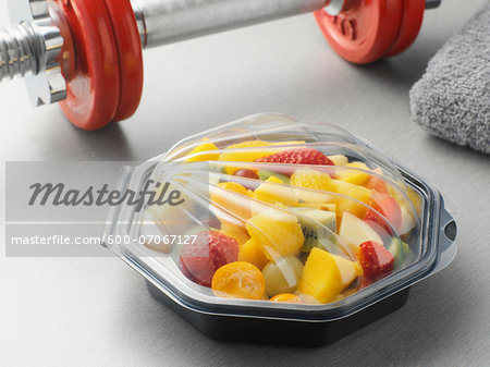 Fruit salad in plastic container with barbell, studio shot Fruit salad in plastic container with barbell, studio shot
