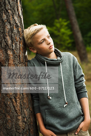 Portrait of boy standing in front of tree in park, looking into the distance, Germany