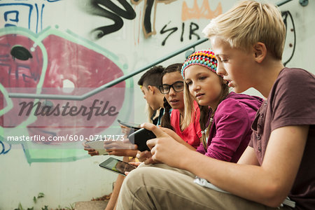 Group of children sitting on stairs outdoors, using tablet computers and smartphones, Germany