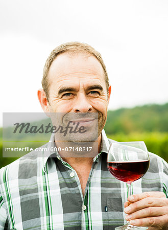 Close-up portrait of vintner standing in vineyard, holding glass of wine, smiling and looking at camera, Rhineland-Palatinate, Germany