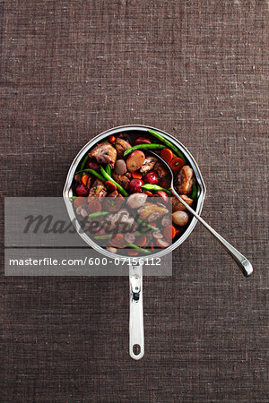 Coq au vin in cooking pot with serving spoon on grey background, studio shot