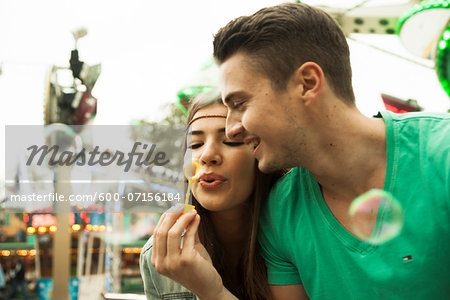 Close-up portrait of young couple blowing bubbles at amusement park, Germany
