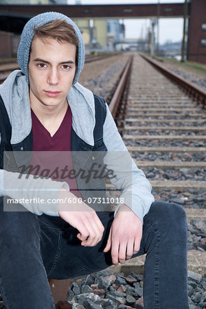 Portrait of teenage boy sitting on railroad tracks, looking at camera, Germany