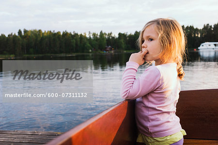 3 year old girl standing in a docked motorboat, looking at the lake, Sweden