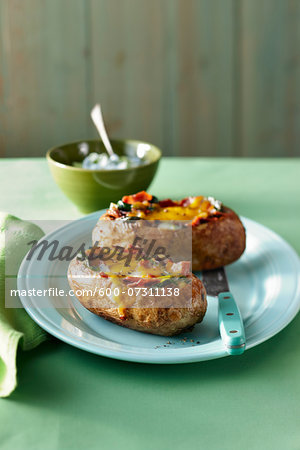 Two stuffed baked potatoes with bacon, spinach, onion and cheddar cheese on a plate on a green tabletop