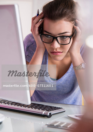 Close-up of young woman using laptop computer, looking confused, studio shot