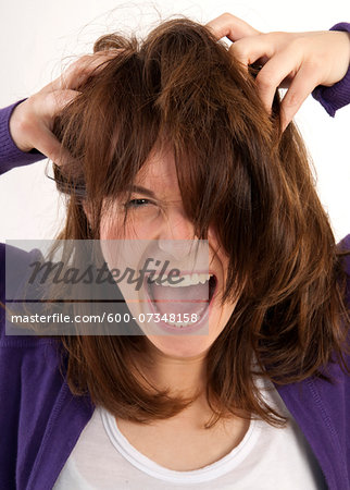 Close-up portrait of young, brown-haired woman screaming and looking at camera with hands in her hair, studio shot on white background Close-up portrait of young, brown-haired woman screaming and looking at camera with hands in her hair, studio shot on white background
