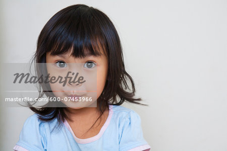 Close-up portrait of Asian toddler girl, looking at camera with surprised expression, studio shot on white background