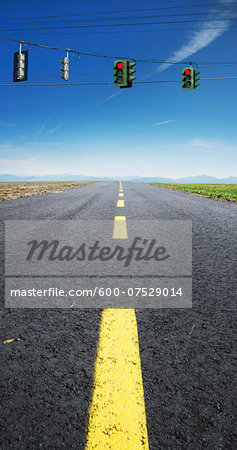 Close-up view of yellow, broken center line on deserted highway, with red traffic lights hanging on wires across road, Canada Close-up view of yellow, broken center line on deserted highway, with red traffic lights hanging on wires across road, Canada