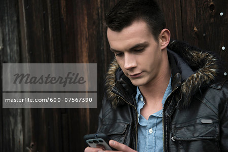 Close-up of young man wearing jacket outdoors and looking at cell phone, Germany