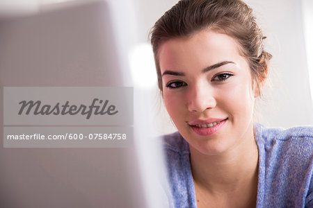 Close-up of young woman working in office on desktop PC, looking at camera and smiling, Germany