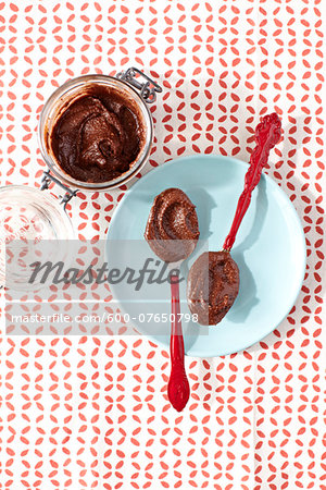 Overhead View of Jar of Hazelnut Paste and Spoons filled with Hazelnut Paste on Plate on Red and White Patterned Background, Studio Shot