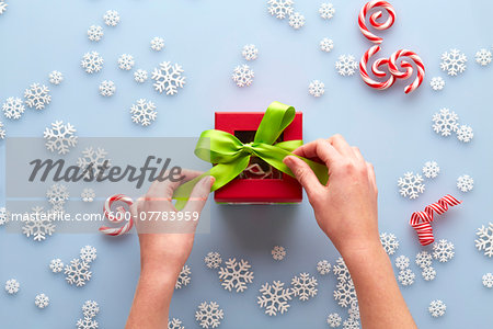 Overhead View of Hands Tying Bow on Present with Snowflakes and Candy Cane Swirls, Studio Shot Overhead View of Hands Tying Bow on Present with Snowflakes and Candy Cane Swirls, Studio Shot