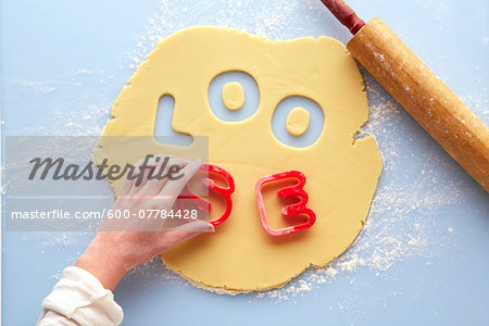 Overhead View of Woman's Hand using Cookie Cutters to spell LOOSE in Rolled out Suger Cookie Dough, Studio Shot
