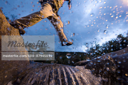 Low angle view of man jumping over a stream while hiking in New Hampshire, USA