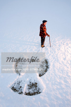 An elderly using a cane, standing in the snow beside a snow angel, New England, USA An elderly using a cane, standing in the snow beside a snow angel, New England, USA
