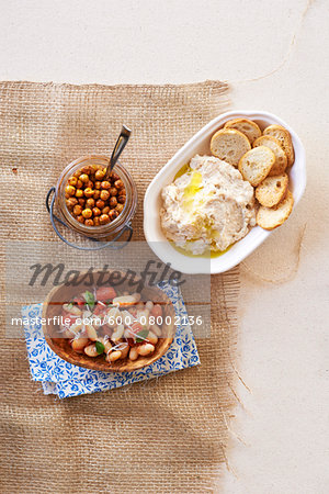 Three bean side dishes, kidney beans, hummus and chick peas in bowls on burlap, studio shot