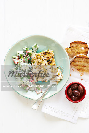 Lemon Cod with Greek Salad and fork on a green plate, with Bread and Olives in bowl on cloth napkin, studio shot on white background Lemon Cod with Greek Salad and fork on a green plate, with Bread and Olives in bowl on cloth napkin, studio shot on white background