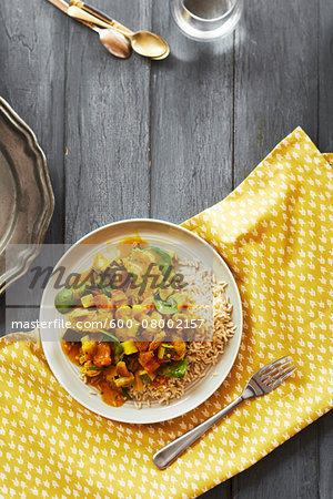 Pork and vegetable curry on rice with a fork on a yellow napkin, studio shot on grey background