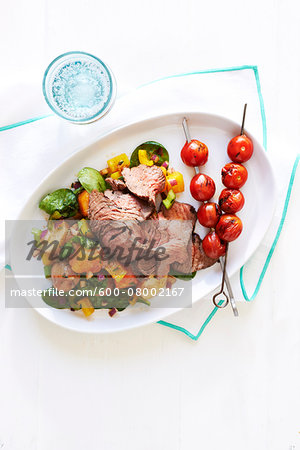 Grilled steak and cherry tomato skewers with potato salad on white plate, studio shot on white background