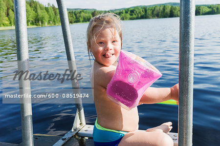 Girl with Down Syndrome wearing Water Wings Sitting on Jetty of Lake, Sweden Girl with Down Syndrome wearing Water Wings Sitting on Jetty of Lake, Sweden