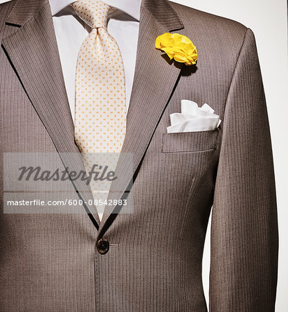 Detail of a light brown suit jacket with cream colored shirt and white handkerchief, yellow patterned necktie and yellow flower