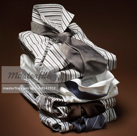 Stack of men's, striped dress shirts with ties on brown background Stack of men's, striped dress shirts with ties on brown background
