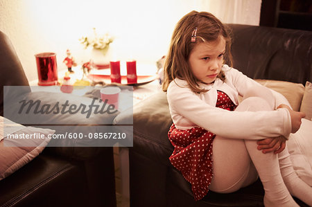 6 year old girl sitting on a sofa at Christmas looking sad, Germany