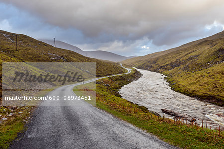 Winding road with river and cloudy sky in the highlands at Glen Coe in Scotland, United Kingdom