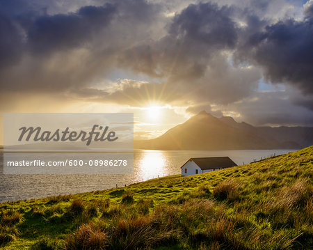 Rooftop of a house along the Scottish coast with sun shining through the dramatic clouds over Loch Scavaig on the Isle of Skye in Scotland, United Kingdom