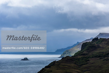 Sunlit ocean with sea cliffs and rain clouds along the coast of the Isle of Skye in Scotland, United Kingdom