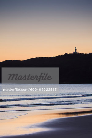 Silhouette of Cape Byron Lighthouse on hilltop and beach at sunset at Byron Bay in New South Wales, Australia