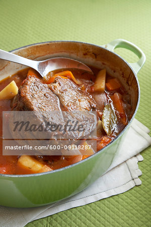 Beef pot roast with root vegetables in an enamel cast iron pot on a green background