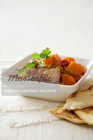 Chicken curry in square bowl, served with pita bread