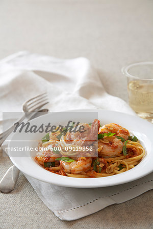 Shrimp linguine on a white plate with linen napkin and a glass of white wine