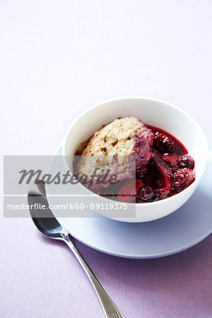 Bowl of berry fruit cobbler with a biscuit topping and a spoon on a purple background
