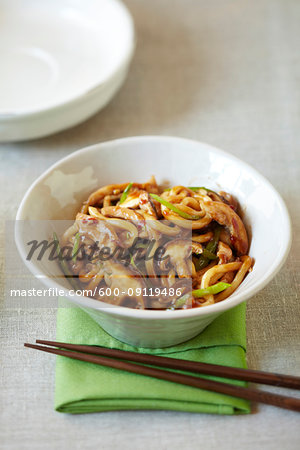 Bowl of udon noodles with shiitake mushrooms, green onions, chili sauce served with chopsticks on a green napkin