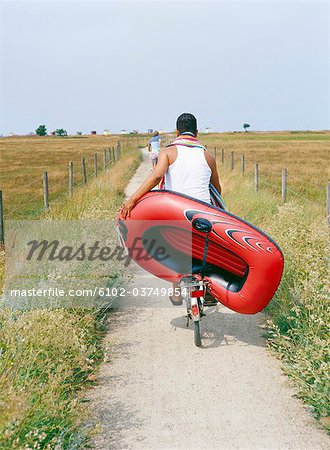 A man cykling carrying a rubber dinghy.