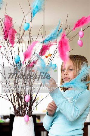 A girl putting easter decorations on a bouquet of twigs.