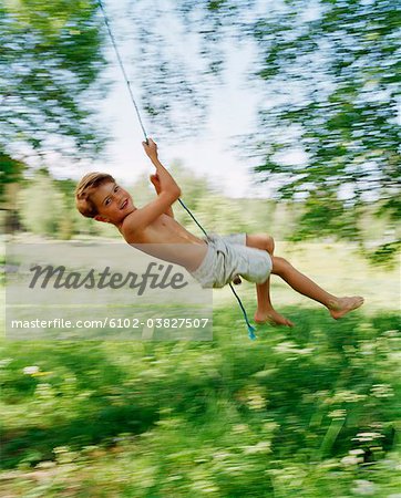 A boy swinging in a green garden.