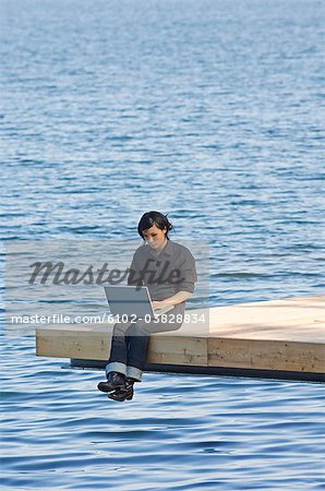 Young woman on a jetty using a laptop, Sweden.