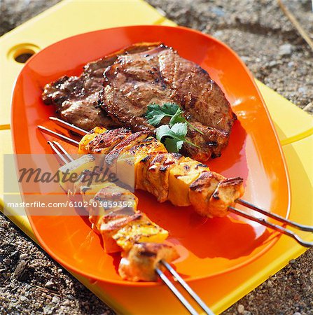 Skewered meat and steak on plate, close-up