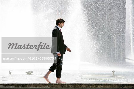 A businessman walking on a wall next to a fountain, Stockholm, Sweden.